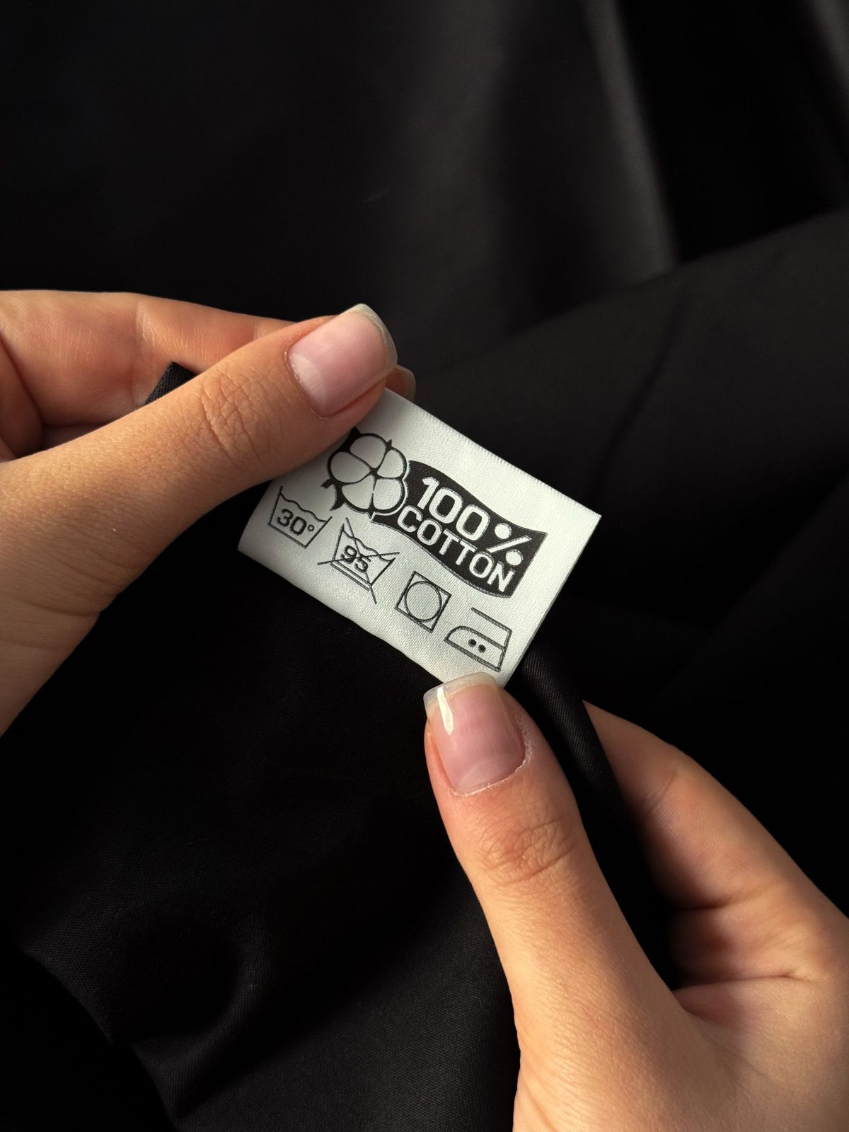 Hands holding a woven fabric care label sewn into a garment